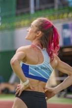 Sportswoman from behind in the stadium, sports outfit, pink hair tied in a braid, middle distance