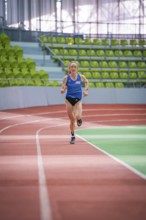 Woman sprinting straight ahead on a red track in the stadium, middle distance runner Katharina
