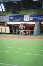 A sporty woman runs at high speed across the green track of a stadium with advertising, middle