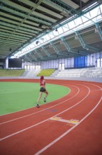 An athlete runs dynamically on a curvy red track in an indoor stadium, middle distance runner