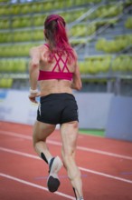 Determined woman running on a running track in a modern hall, middle distance runner Katharina