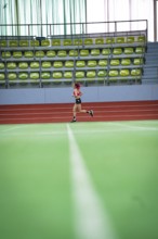 Female athlete running alone on an extensive track in a hall, middle distance runner Katharina