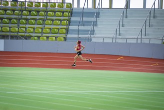 Woman running fast on a red track with strong concentration, middle distance runner Katharina
