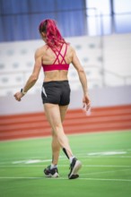Female athlete in sports hall on synthetic track in dynamic posture, middle distance runner