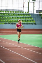 Sporty dressed woman running on an indoor track, showing speed and focus, middle distance runner