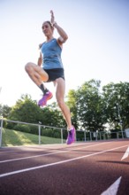 A sporty person jumps with momentum on the track in a blue outfit and pink shoes, middle distance