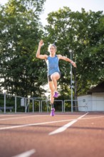 Female athlete wearing a blue outfit jumps dynamically on the track in lively surroundings, middle