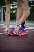 Close-up of person lacing pink running shoes on track with wristwatch, middle distance runner