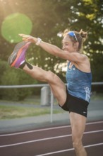 On the track, woman performs a high kick in the evening sun, middle distance runner Katharina