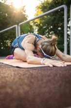Woman stretching on a mat, lying relaxed in the warm light of sunset, middle distance runner