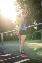 Woman standing on a running track while stretching, raised in sunlight, middle distance runner