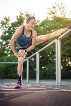 Woman doing intensive stretching on track in sunshine, middle distance runner Katharina Jaiser,