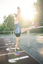 Woman stretches leg on track against bright sunshine, focus on stretching, middle distance runner