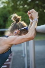 Female athlete in warm-up leaning against a barrier. Focused and concentrated atmosphere, middle