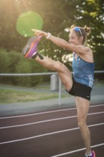 Energetic woman on a running track with a high kick in sunlight, middle distance runner Katharina