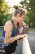 Woman smiling as she stretches her leg on a running track surrounded by summer nature, middle