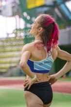 Female athlete with pink hair in the stadium, looking up. Determined atmosphere, middle distance