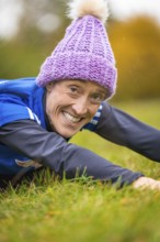Woman lying on grass smiling, relaxed and satisfied in colorful winter clothes, middle distance