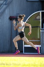 A woman in sporty clothes runs fast on a track in a stadium, middle distance runner Katharina
