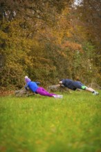 Two people doing push-ups on rocks in an autumnal forest, middle distance runner Katharina Jaiser,