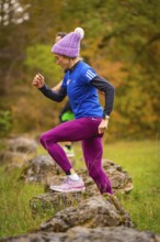Woman in sporty clothing climbs energetically on rocks in autumn nature, middle distance runner