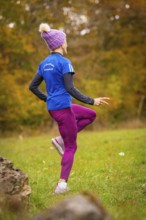 Woman wearing pink sports pants and blue jacket training in autumn forest, middle distance runner