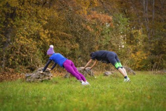 Two people working out outdoors doing push-ups on rocks in an autumn forest, middle distance runner