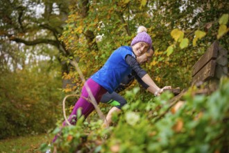 Woman wearing colorful sportswear smiles during a workout in autumn forest, middle distance runner