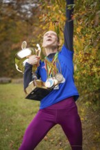 Woman with cup and medals cheers wildly in autumn, middle distance runner Katharina Jaiser,