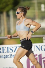 Side view of female athlete running in sporty clothes in warm weather, middle distance runner