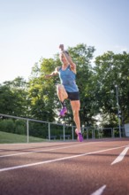 Athlete jumping on a track surrounded by green trees and bright sunshine, middle distance runner