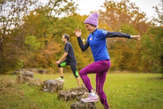 Two people jump off rocks during sporting activity in autumn forest, middle distance runner