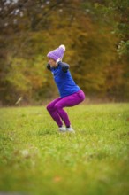 Woman wearing colorful sportswear doing jumping exercises on an autumnal meadow, middle distance