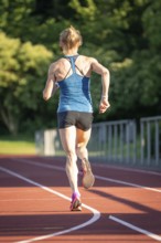 Back view of a running athlete on a red track surrounded by nature, middle distance runner