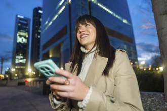 Young professional woman smiling and looking away while interacting with a smartphone in a modern