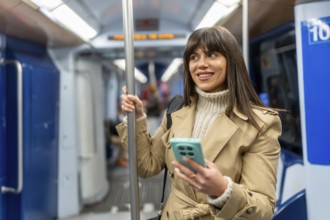 Young woman standing inside a modern subway train, holding onto a pole while checking her