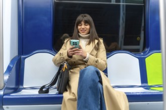 Young woman sitting on a subway train, actively engaging with her smartphone during a daily