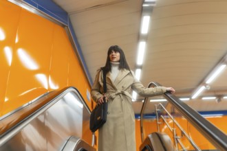Woman travelling on an escalator in a subway station, holding onto the handrail, dressed in a