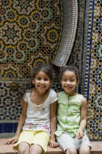 Two smiling girls in front of a wall with colorful tiles, alley in the old town, Souk, Fez El Bali,
