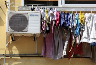 The laundry hangs to dry on a line in front of the window, next to it an air conditioner, typical