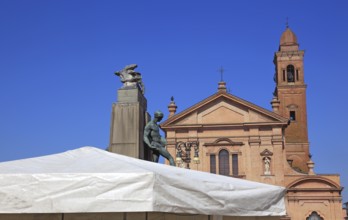 Monument with a statue in Piazza Unita and the Santo Stefano Collegiate Church in the city of