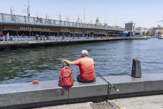 Istanbul, Turkey. June 23rd 2025. A mam sits fishing on the dockside in Eminonu beside the famous