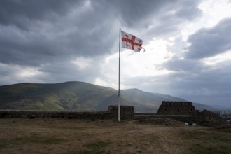 Dramatic heavy clouds and the Georgian flag over the mountain landscape surrounding Gori city