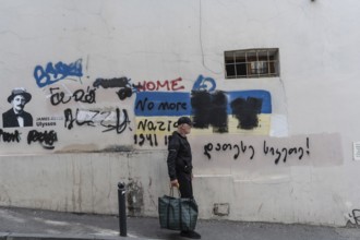 Tbilisi, Georgia. July 7th 2025. An elderly local man walks past a wall of graffiti in a side