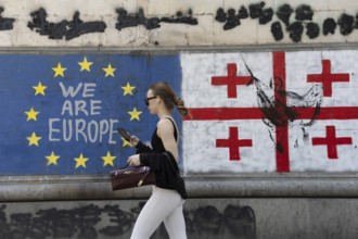 Tbilisi, Georgia. July 7th 2025. A woman walks past the flags of Georgia and the European Union