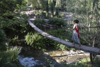 Tbilisi, Georgia. July 13th 2025. A foreign tourist crosses a wooden rope bridge inside the