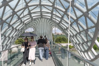 Tbilisi, Georgia. July 7th 2025. Tourists cross The Bridge of Peace over the Kura River in the