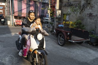 Bangkok, Thailand. March 18th 2025. A mother with her daughter rides a motor scooter through the