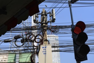 A red traffic light with a tangled mess of cables and wires with mobile communication mast, Bangkok