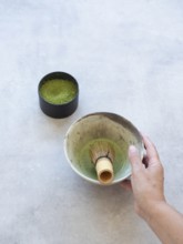 Hand holding a traditional japanese chawan with matcha and bamboo whisk